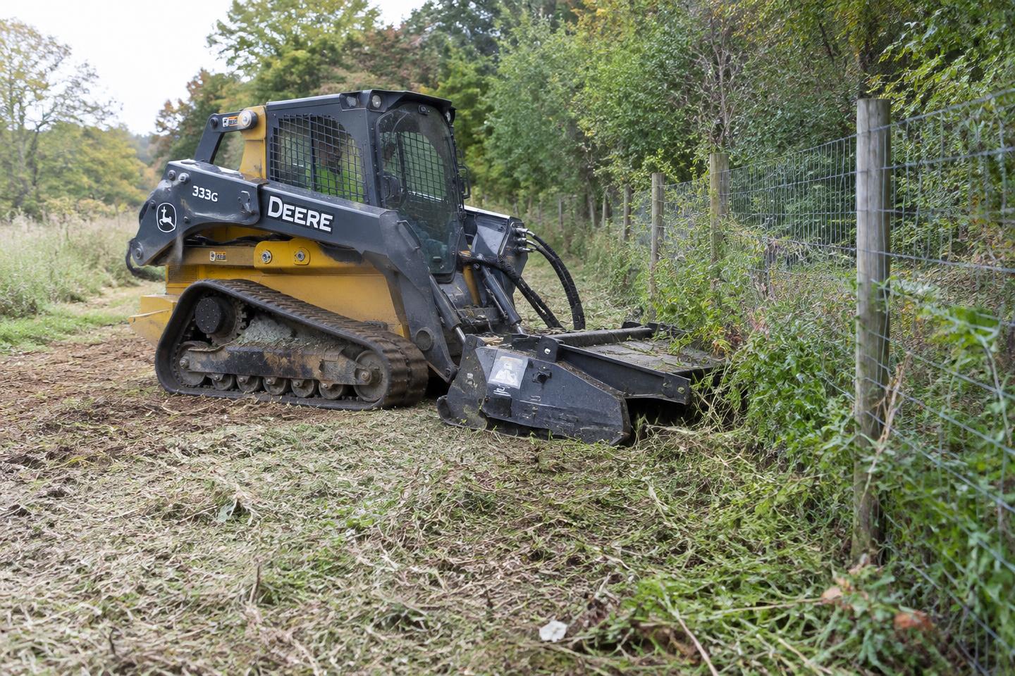 Track loader with brush cutter clearing overgrowth along a fence line — sample imagery